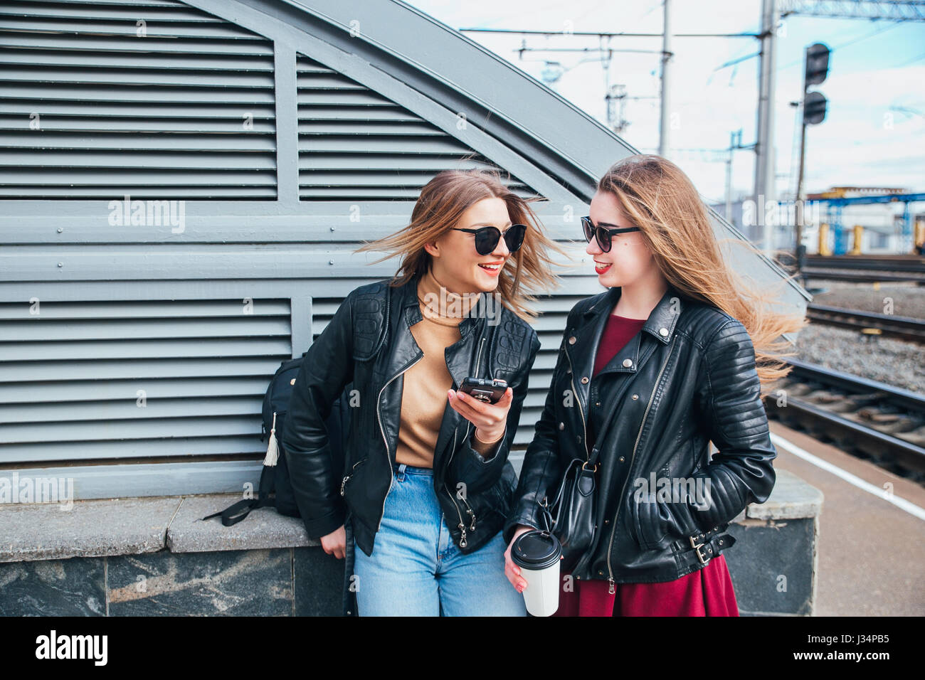 Two Women Talking in the City.Outdoor lifestyle portrait of two best friends hipster girls wearing stylish Leather Jacket and sunglasses with cofee, going crazy and having great time together Stock Photo