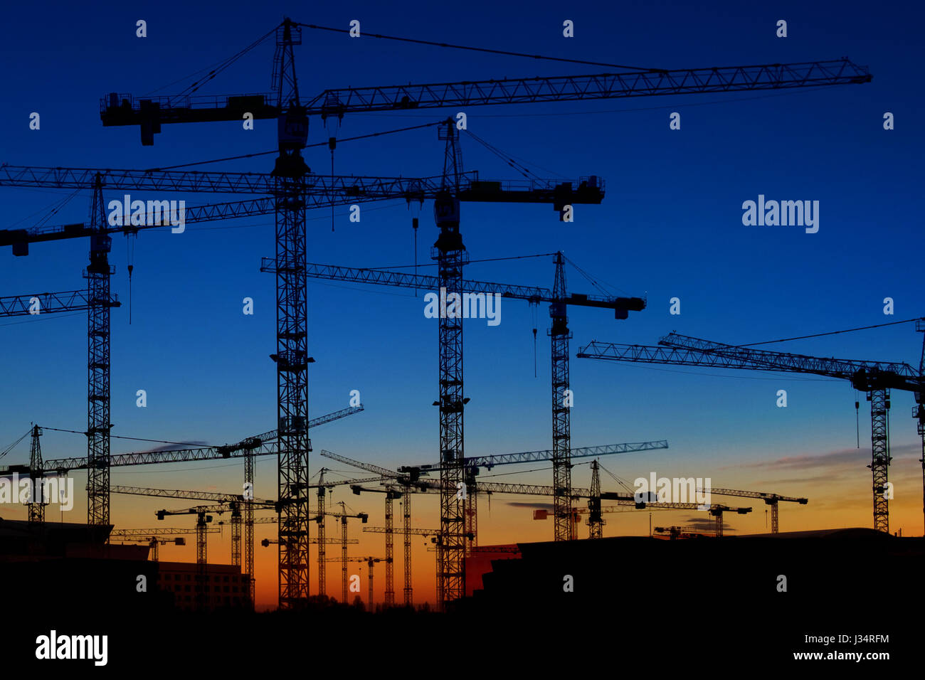 many construction cranes on sunset sky - crane silhouette skyline Stock Photo
