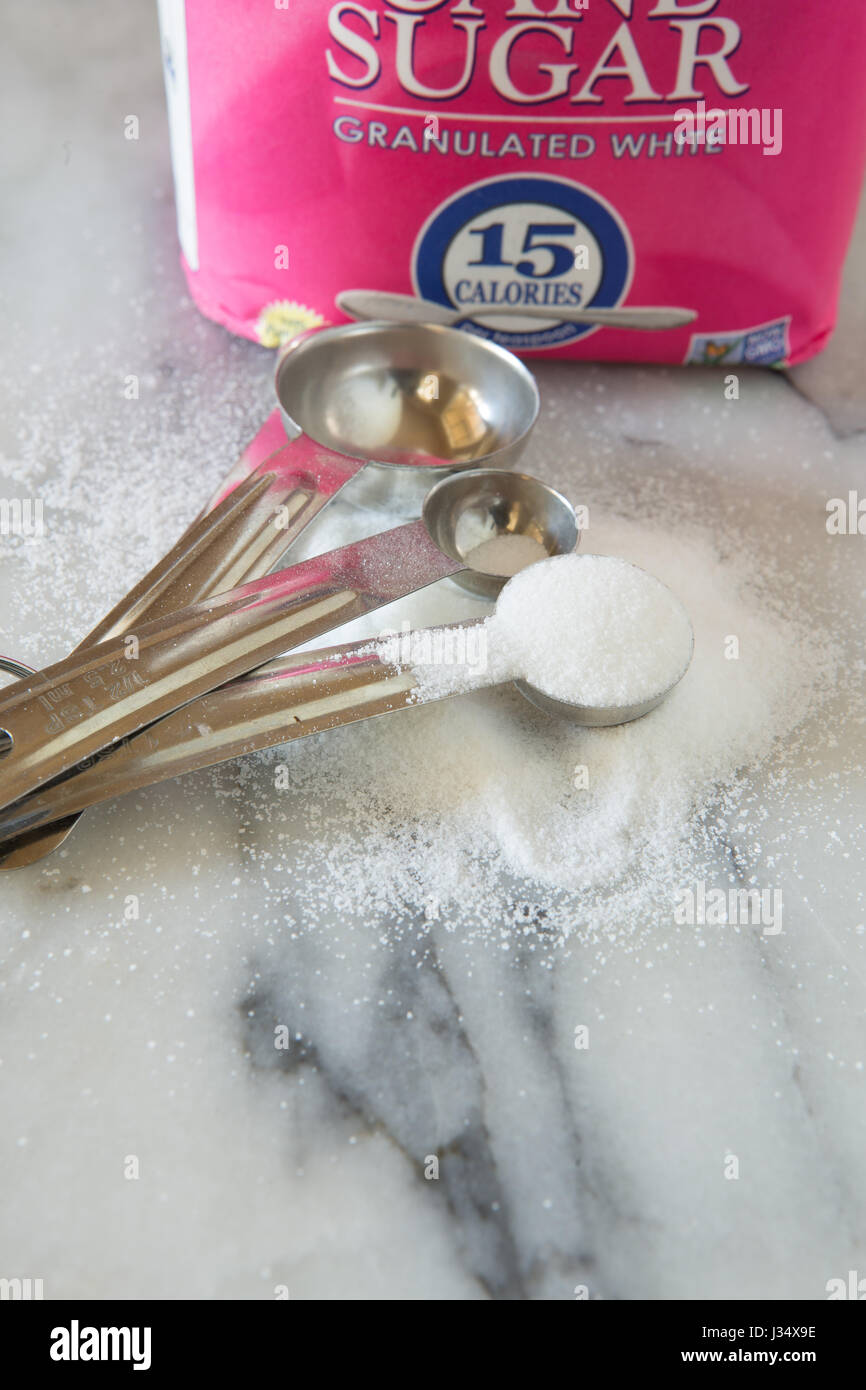 A teaspoon of granulated white cookery in a home kitchen on a marble counter top Stock Photo