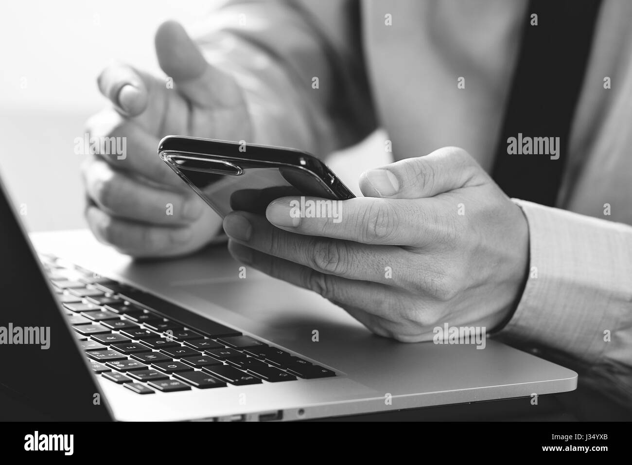 close up of businessman working with mobile phone and laptop computer on wooden desk in modern office,black and white Stock Photo