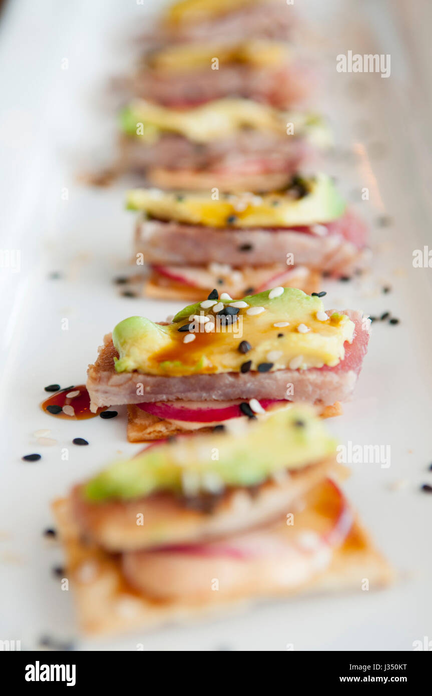 Closeup of ahi tuna appetizer, with avocado and radish on crackers, served on a white plate