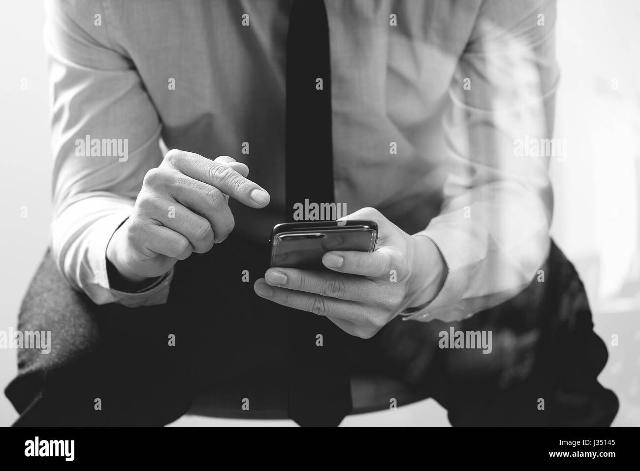 close up of businessman working with mobile phone and sitting on the chair in modern office,black and white Stock Photo