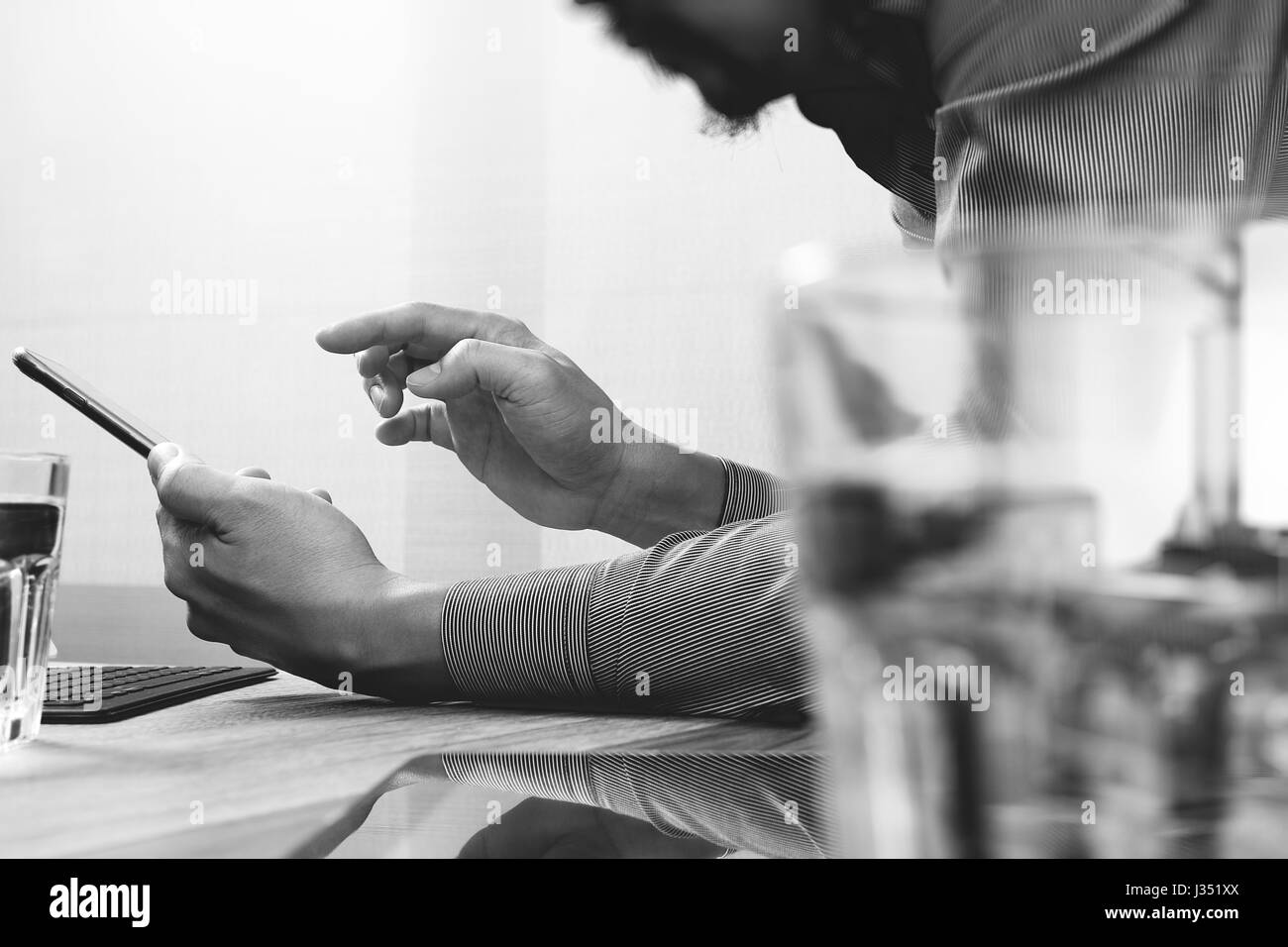 Businessman hand using mobile payments online shopping,omni channel,laptop computer on wooden desk,black white Stock Photo