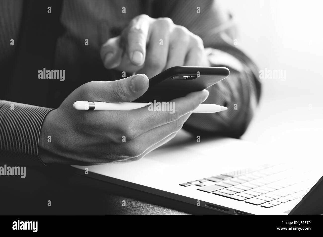 close up of businessman working with mobile phone and stylus pen and laptop computer on wooden desk in modern office,black and white Stock Photo