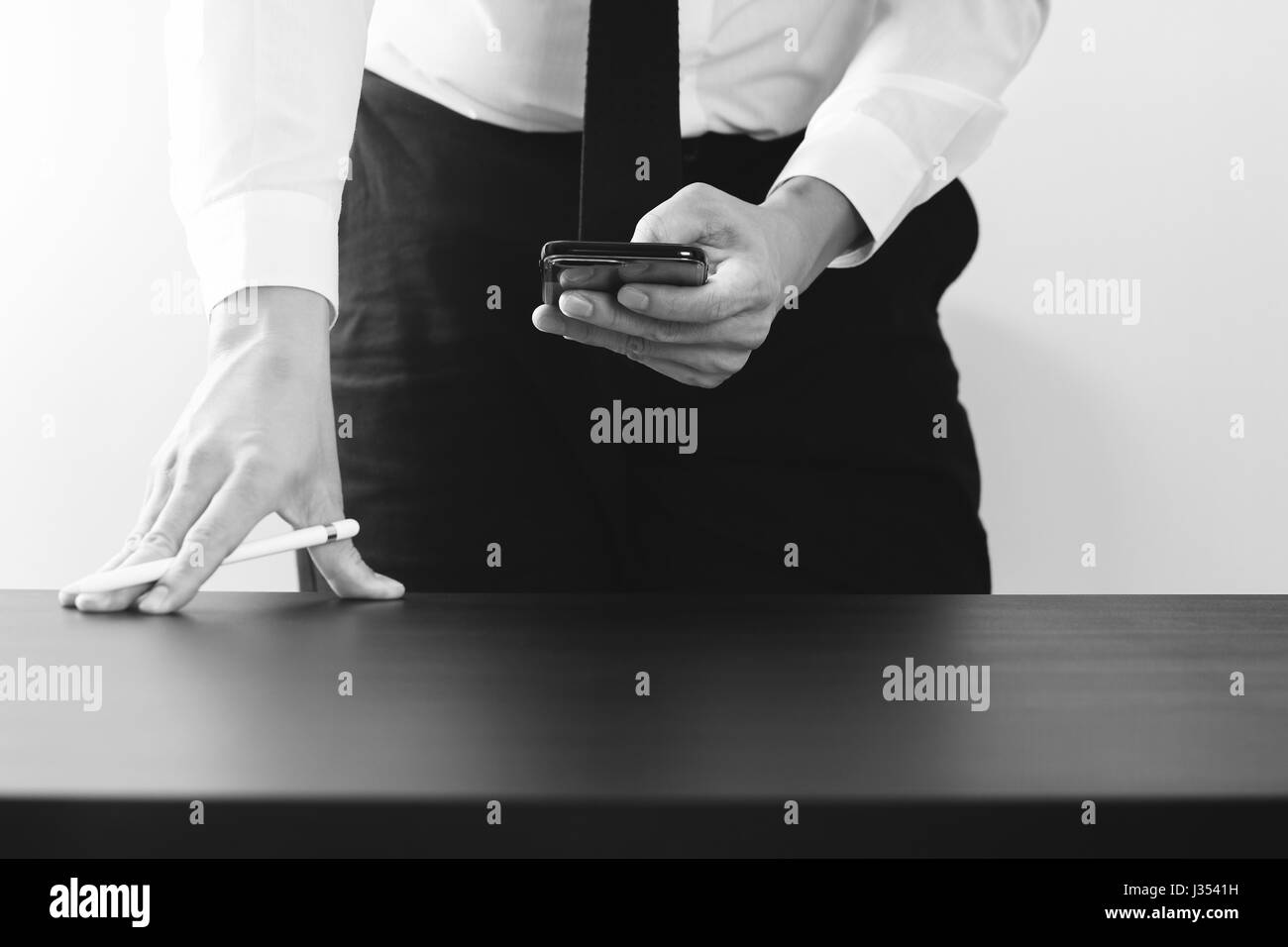 close up of businessman working with smart phone on wooden desk in modern office,black and white Stock Photo