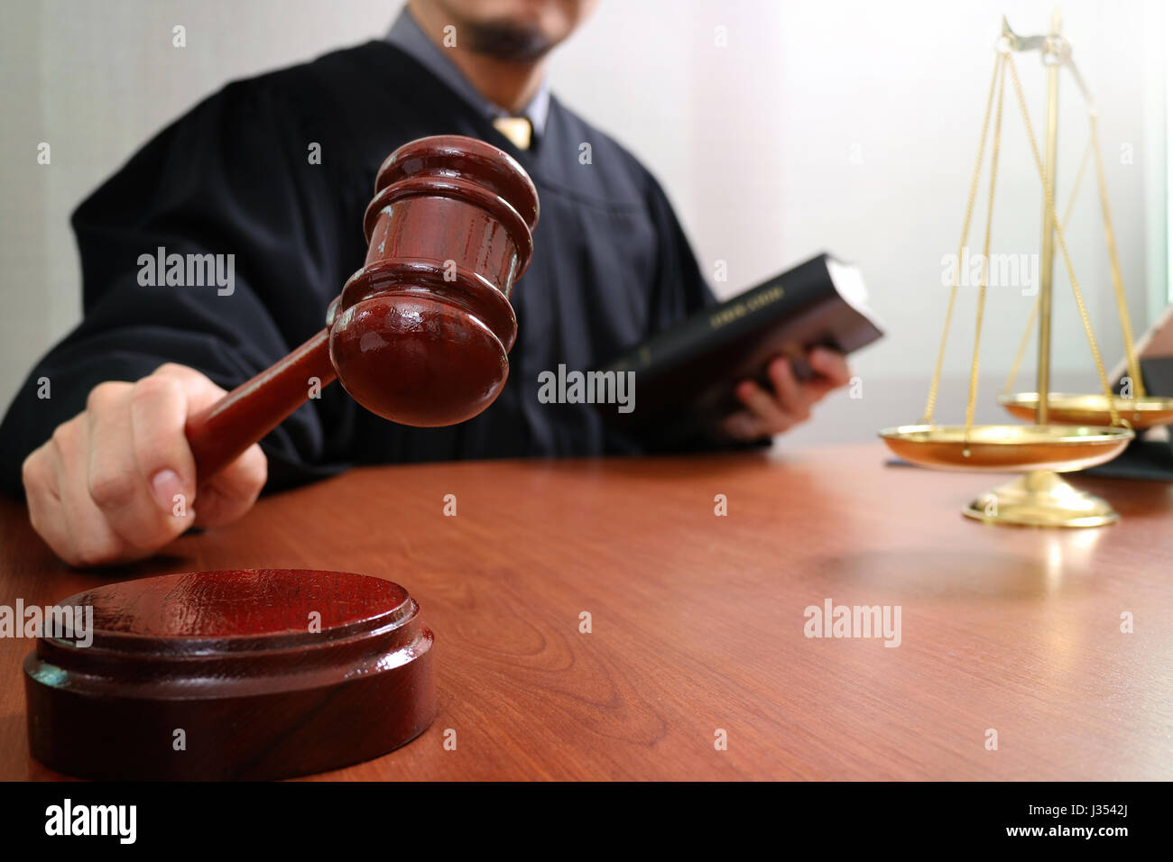 justice and law concept.Male judge in a courtroom with the gavel and working with smart phone and brass scale on wood table Stock Photo