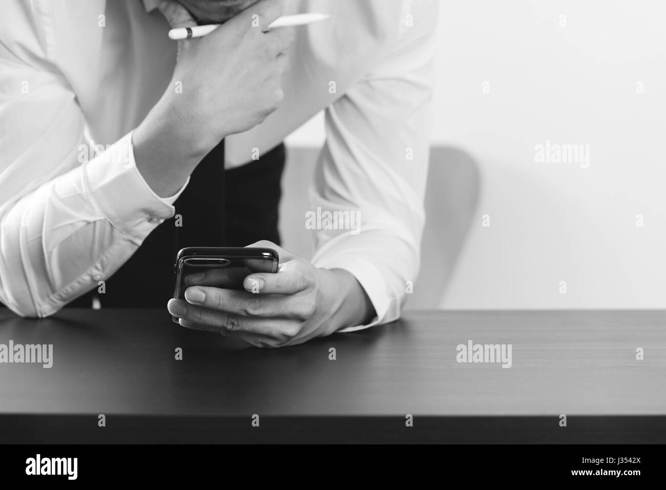 close up of businessman working with smart phone on wooden desk in modern office,black and white Stock Photo