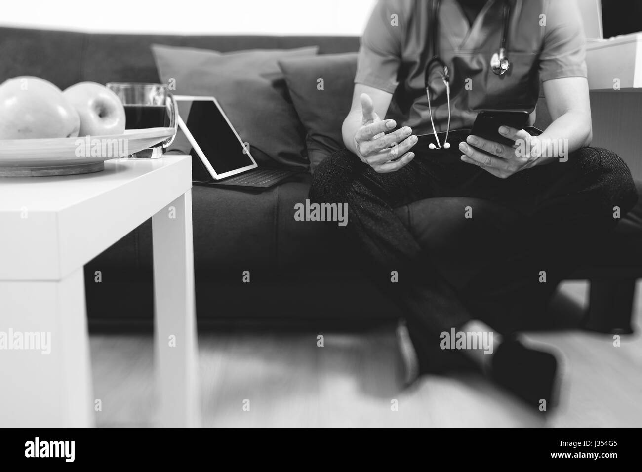 Medical and Health context,doctor hand working with smart phone,digital tablet computer,stethoscope,sitting on sofa in living room,black and white Stock Photo