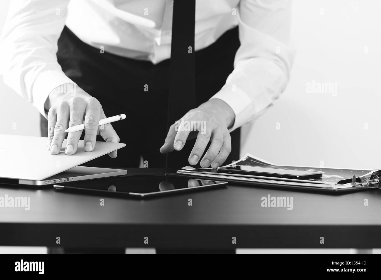 close up of businessman working with smart phone and digital tablet and laptop computer on wooden desk in modern office,black and white Stock Photo