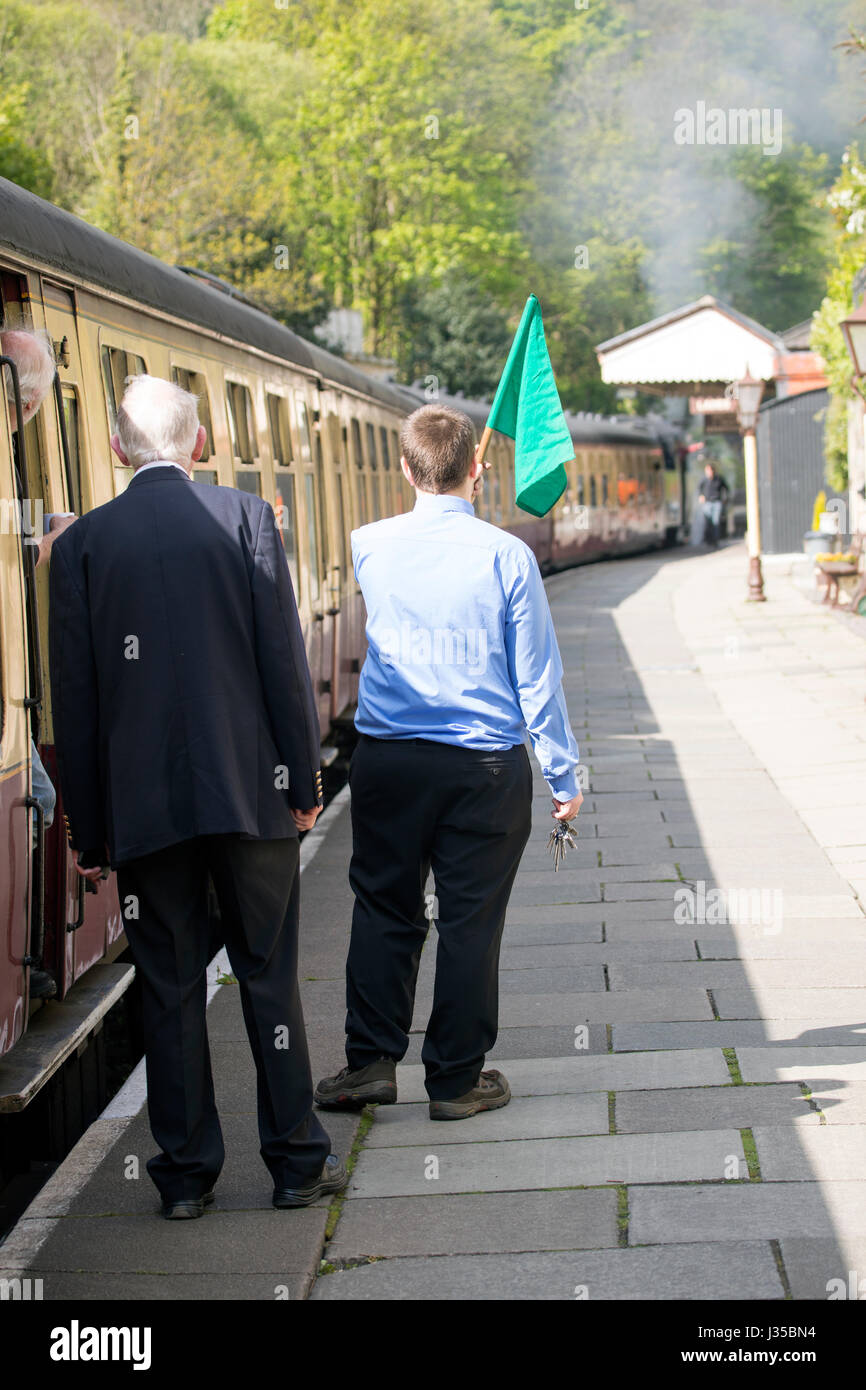 Llangollen steam train conductor waving flag to the driver to begin the train journey along in summer, Llangollen, Denbighshire,Wales Stock Photo