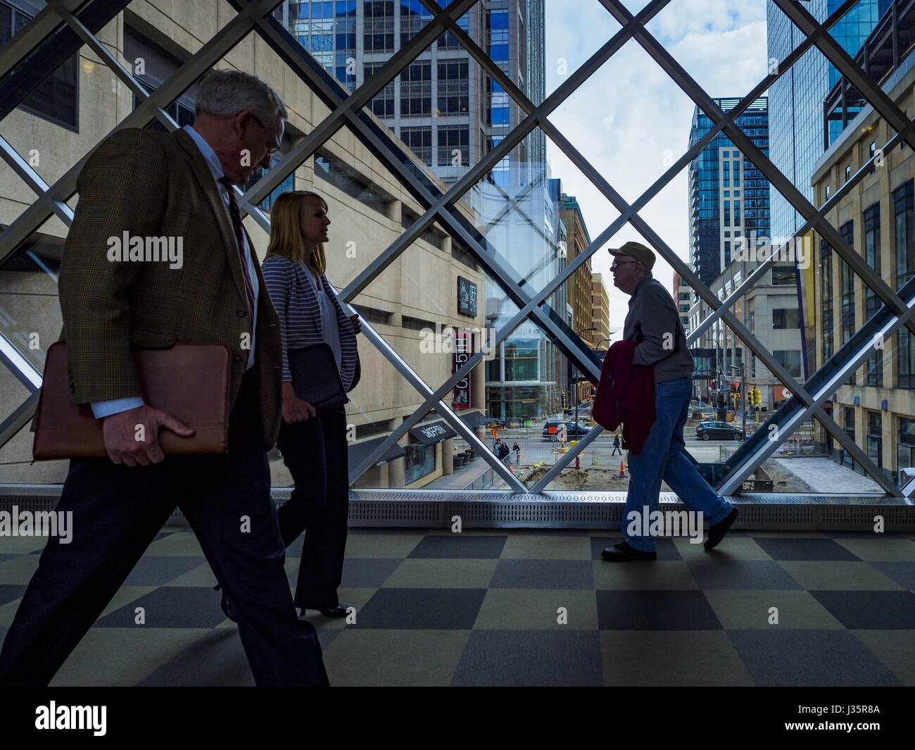 May 3, 2017 - Minneapolis, Minnesota, U.S - People in the skyway over 5th Street in downtown Minneapolis. The skyways are enclosed pedestrian overpasses that connect downtown buildings. The Minneapolis Skyway was started in the early 1960s as a response to covered shopping malls in the suburbs that were drawing shoppers out of the downtown area. The system grew sporadically until 1974, when the construction of the IDS Center and its center atrium, called the Crystal Court, served as a hub for the downtown skyway system. There are 8 miles of skyways, connecting most of the downtown buildings fr Stock Photo