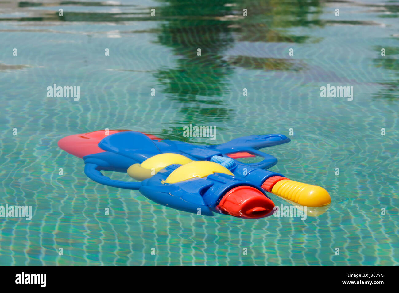 Colorful squirt gun floating in a swimming pool with green tiles floor