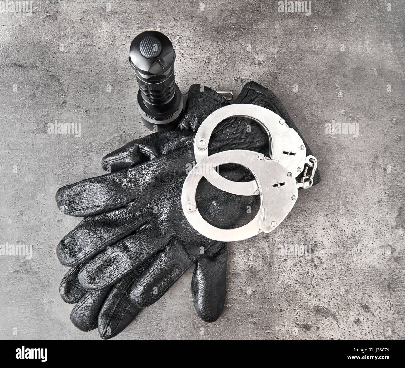 German police handcuffs, leather gloves and a torchlight on rough grey background with copy space. Top down View. Stock Photo
