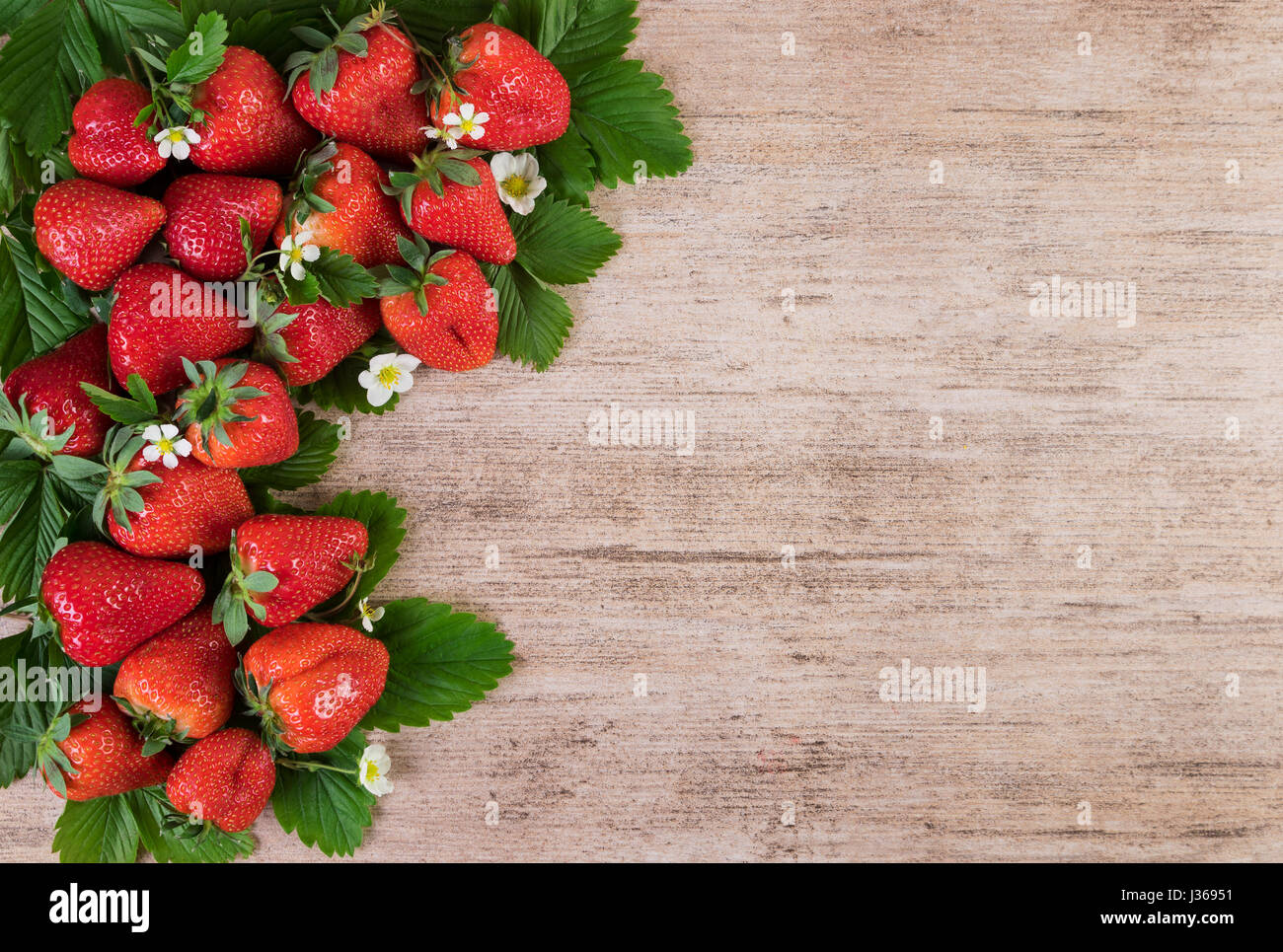 Fresh strawberries with leaves over wooden background with copy space ...