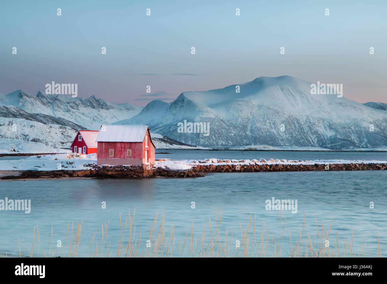 Solitary typical Norwegian red wooden boat house in the snow at sunset Stock Photo