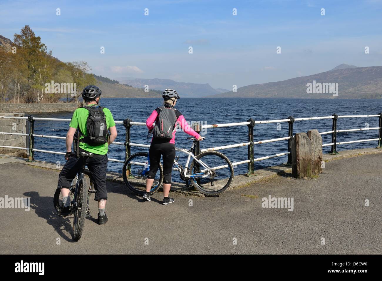 Two cyclists reach the pier at Stronachlachar overlooking Loch Katrine which is a freshwater loch in the Trossachs area of Scotland, UK Stock Photo