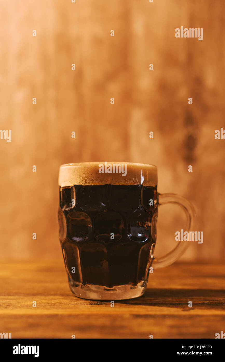 Dark beer in british dimpled glass pint mug on bar table Stock Photo