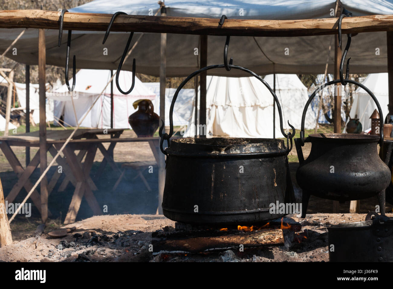 Black cauldrons hang on hooks over the open fire in a medieval camp
