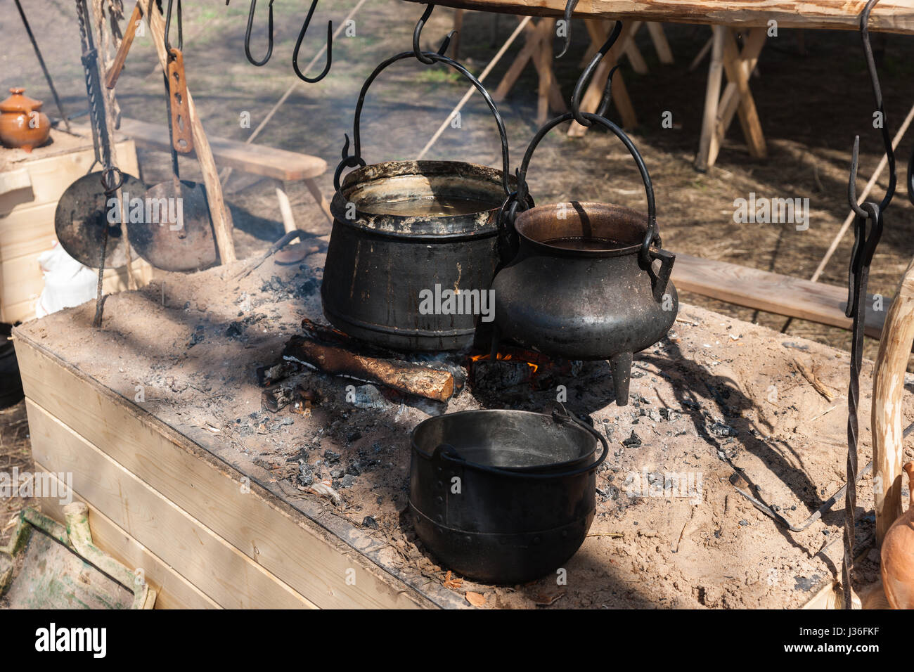 Black cauldrons hang on hooks over the open fire in a medieval camp