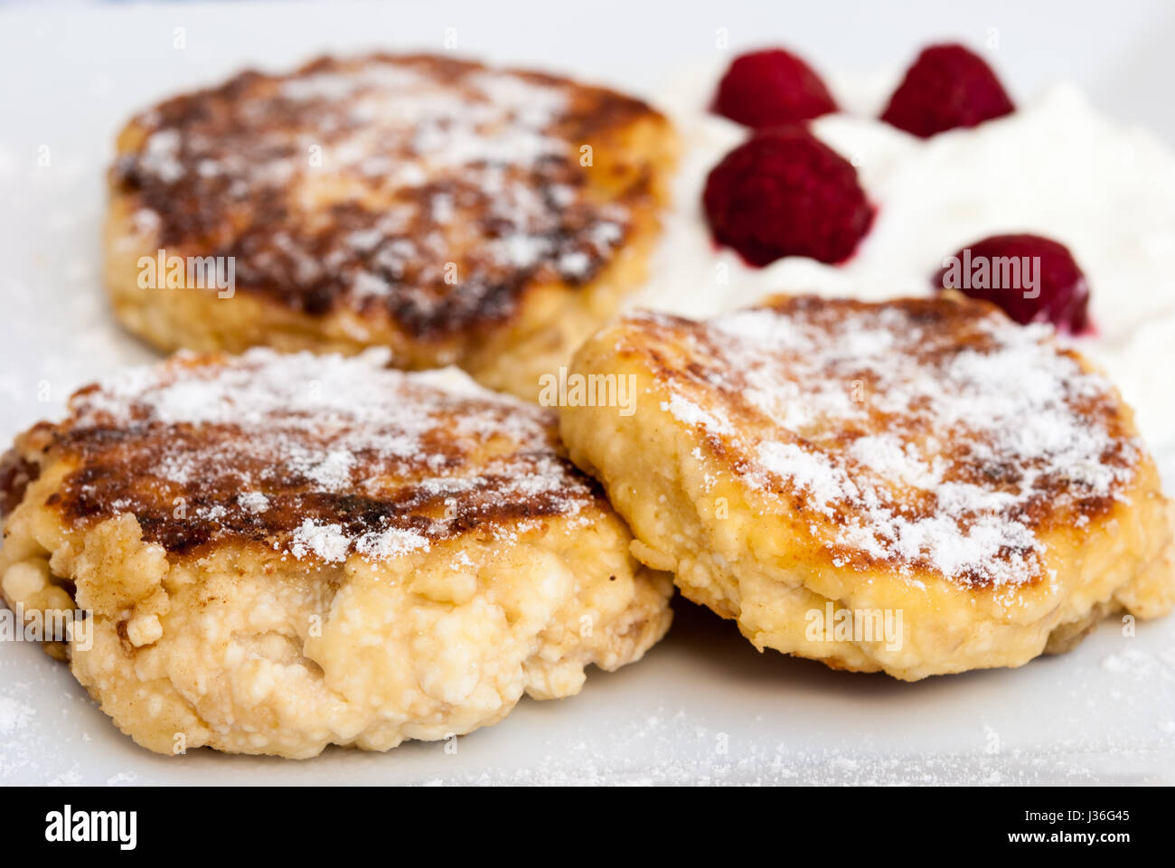 Syrniki (Russian and Ukrainian pancakes) served with sour cream and raspberries Stock Photo