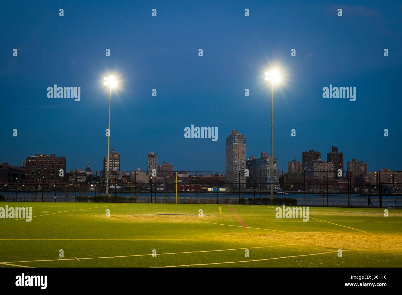 Illuminated soccer field at night with skyline of New York City Stock