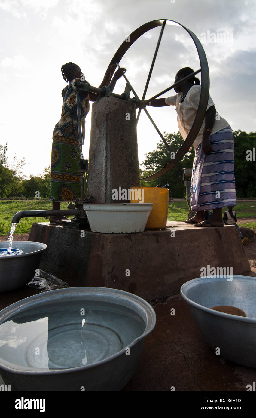 BURKINA FASO, Gaoua , women fetch drinking water from water pump with turning wheel in village / Burkina Faso, Gaoua, Frauen holen Wasser von einem Brunnen mit Drehpumpe Stock Photo