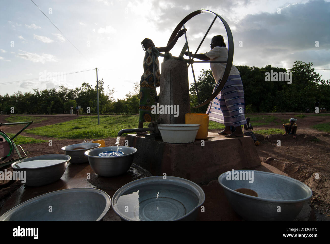BURKINA FASO, Gaoua , women fetch drinking water from water pump with turning wheel in village / Burkina Faso, Gaoua, Frauen holen Wasser von einem Brunnen mit Drehpumpe Stock Photo