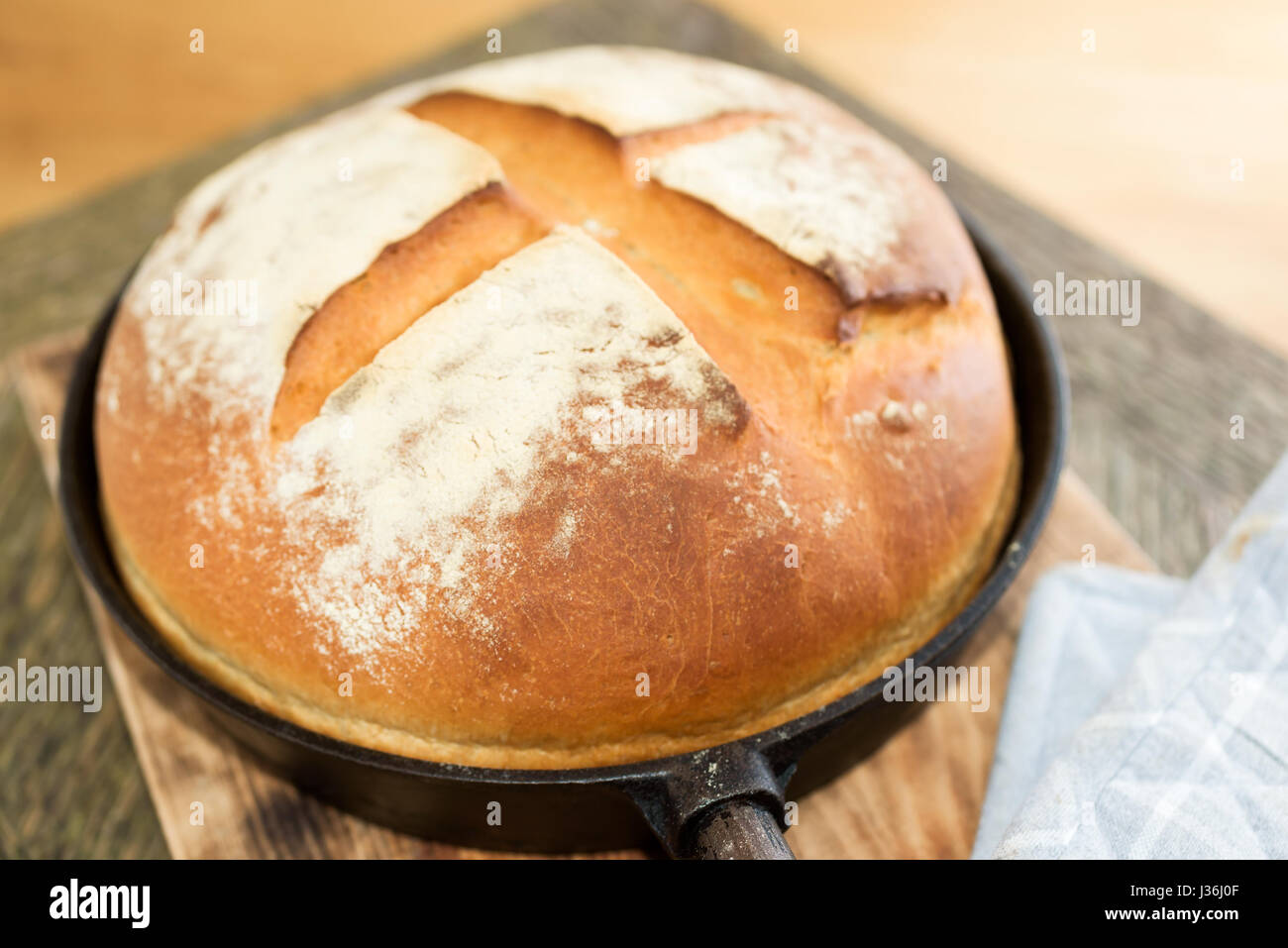 Newly baked artisan bread in cast iron skillet on wooden cutting board. Gray potholder at side. Stock Photo