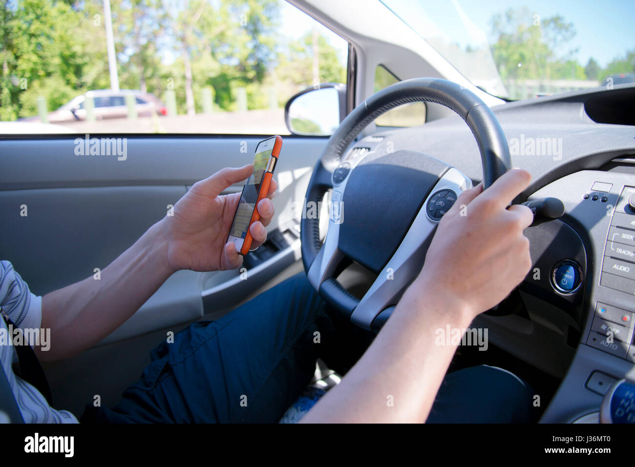 The driver behind the wheel of a car with a phone in his hand sends a text message while driving along the road that could lead to an emergency Stock Photo