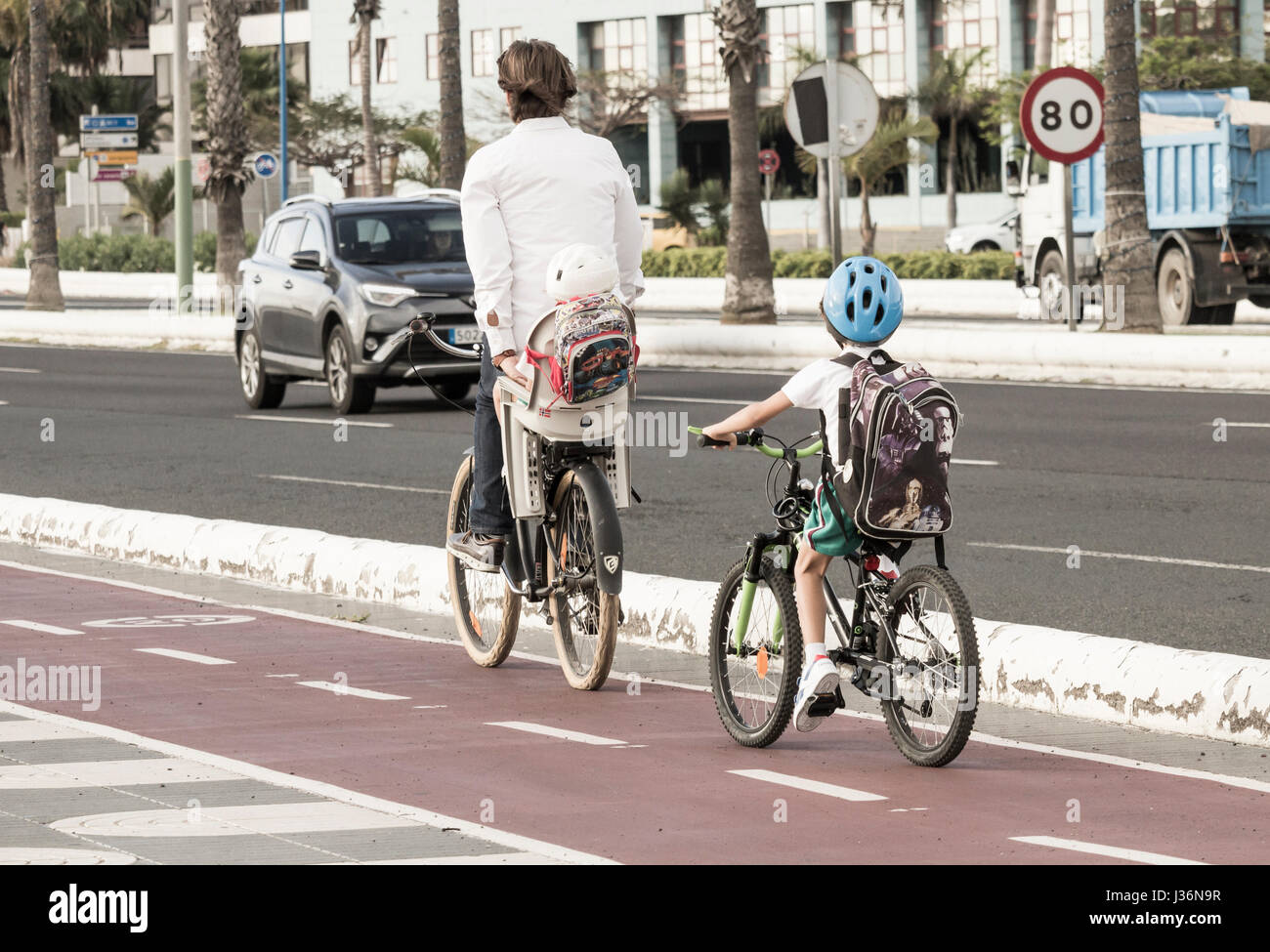 Young boy in school uniform riding to school on bicycle behind adult who is carrying small child. Stock Photo