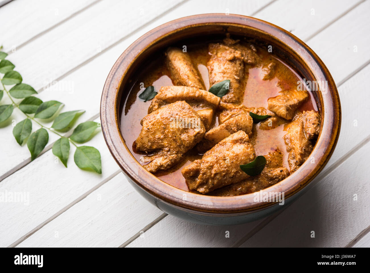 tasty fish curry served with white cooked basmati rice with curry leaves in the background