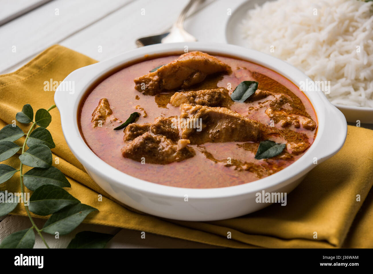 tasty fish curry served with white cooked basmati rice with curry leaves in the background