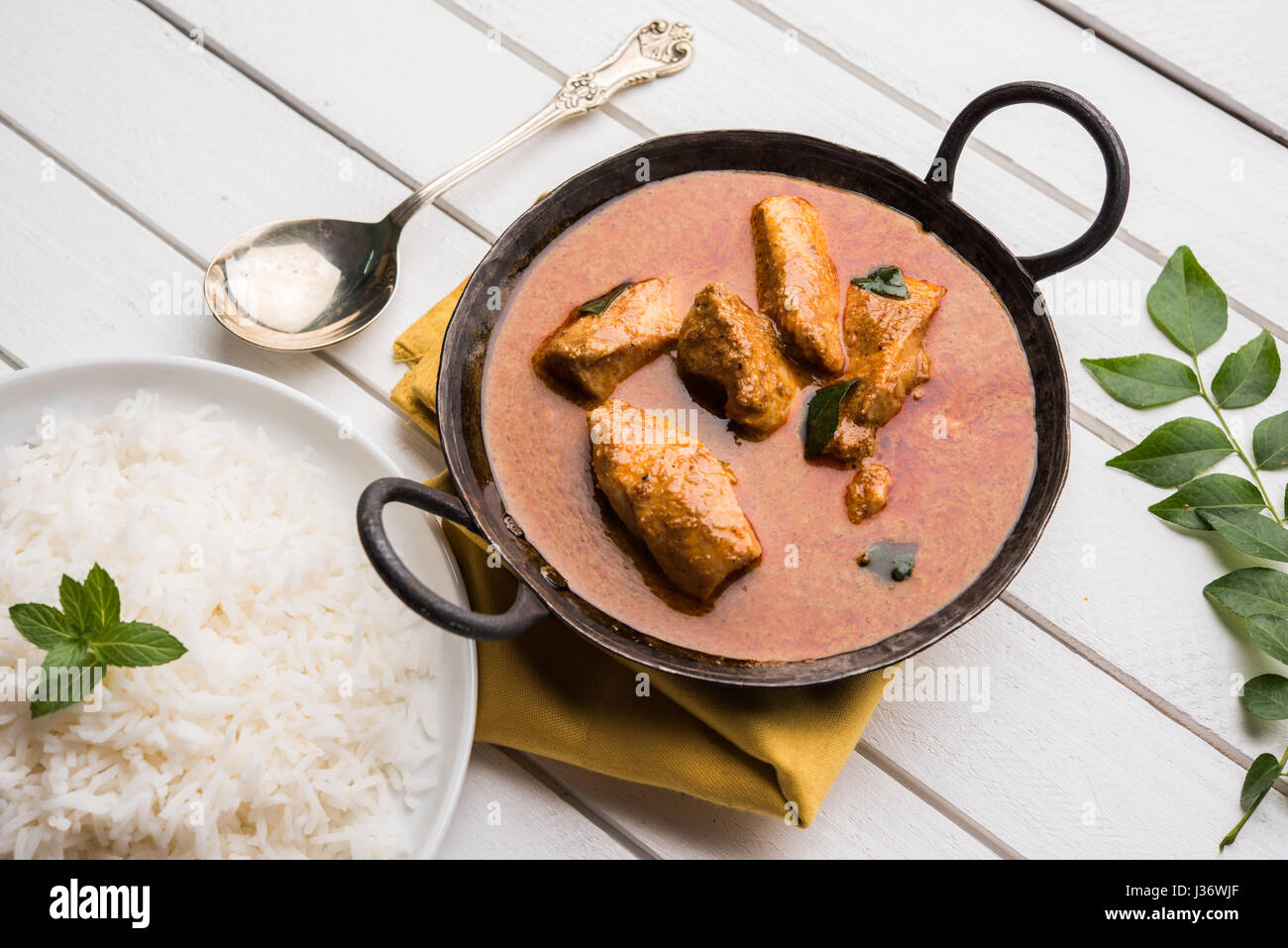 tasty fish curry served with white cooked basmati rice with curry leaves in the background