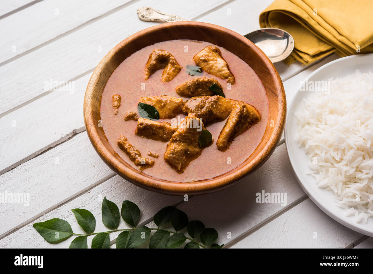 tasty fish curry served with white cooked basmati rice with curry leaves in the background