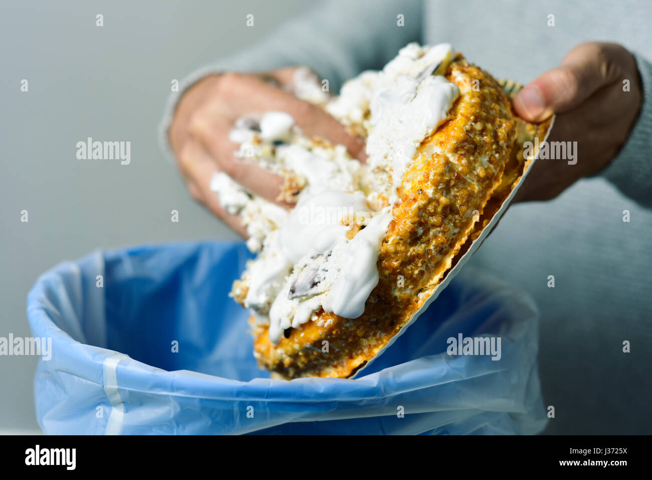 closeup of a young caucasian man throwing a cake topped with whipped cream to the trash bin