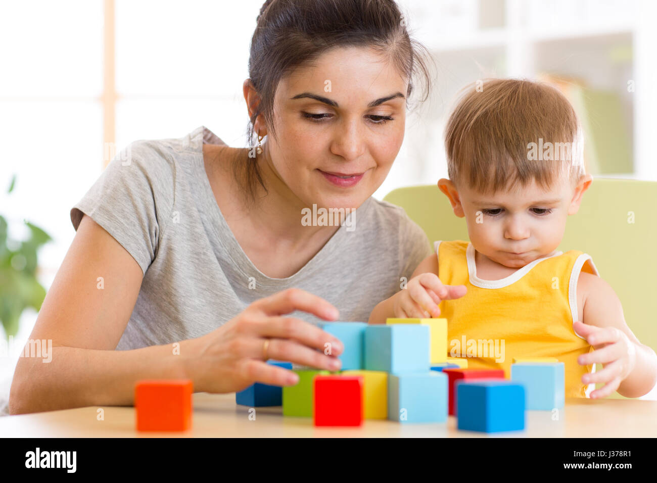 Young mummy and her kid play with cubes toys in nursery Stock Photo