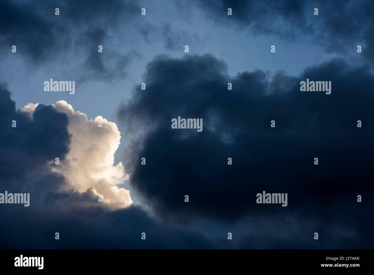 Cumulonimbus clouds at dawn with sun hitting one cloud highlighting it behind the other dark clouds Stock Photo