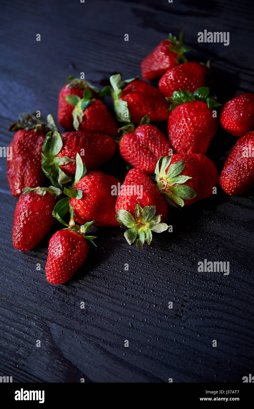 Red juicy strawberry on a dark black wooden background. The droplets of ...