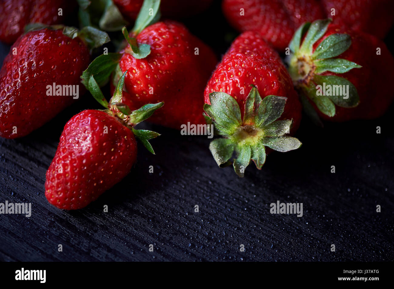 Red juicy strawberry on a dark black wooden background. The droplets of ...