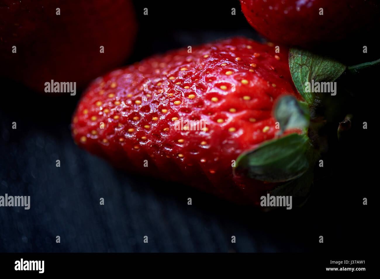 Red juicy strawberry on a dark black wooden background. The droplets of ...