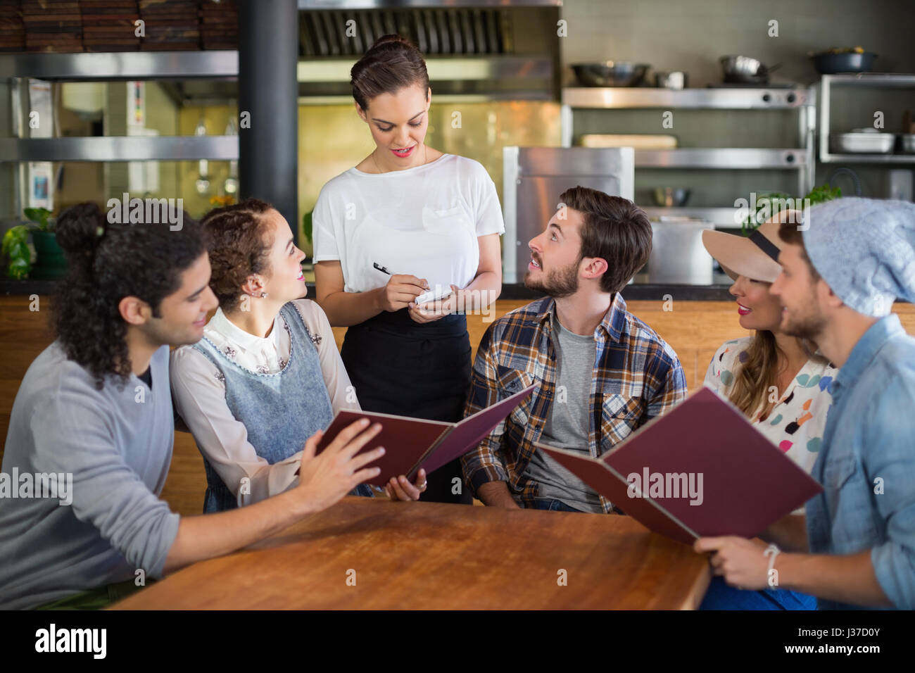 Customers looking at waitress taking down orders in restaurant Stock Photo