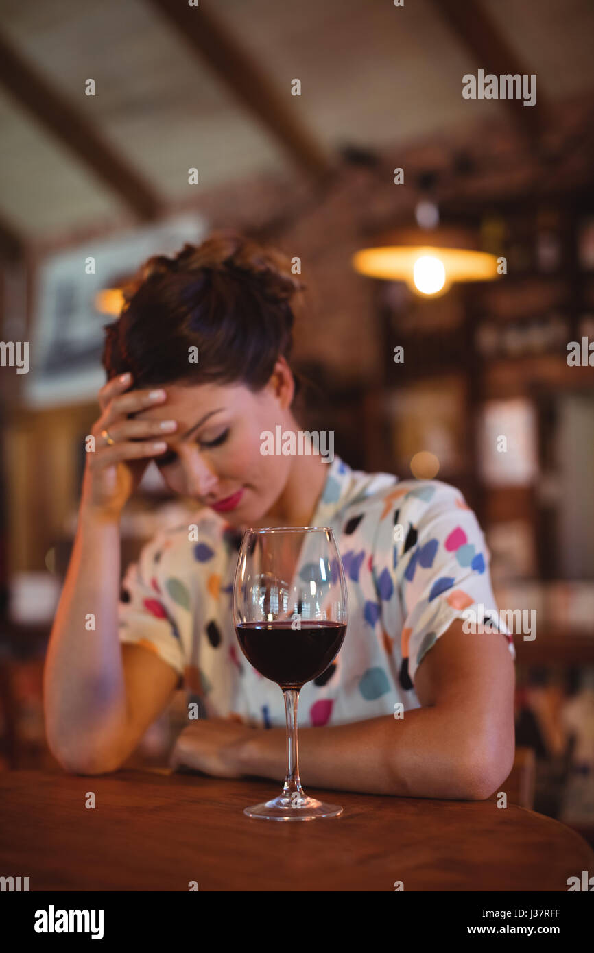 Upset woman sitting with hands on forehead in pub Stock Photo