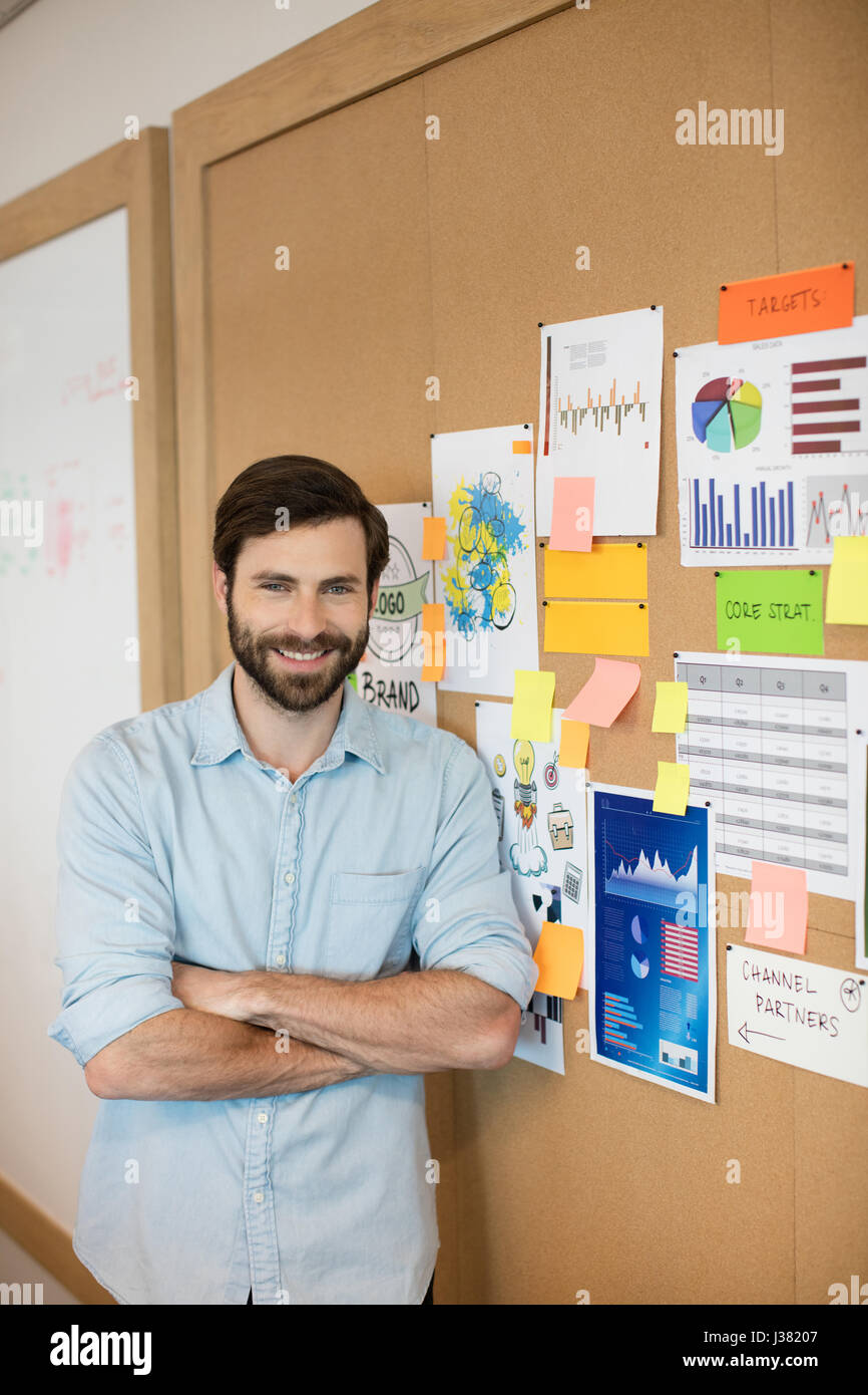 Portrait of confident businessman with arms crossed standing by charts ...