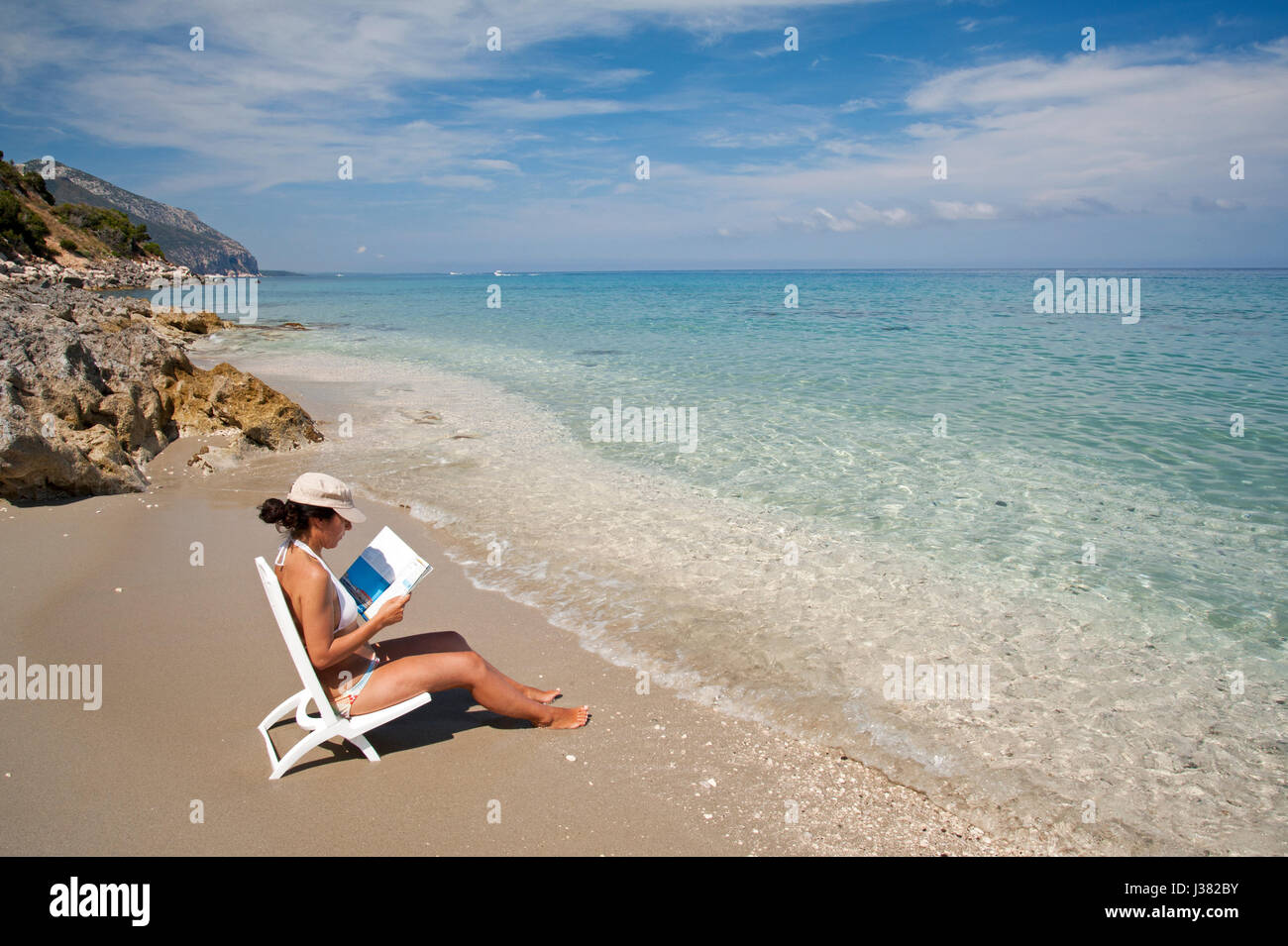 Girl reading book on the shore of Ziu Martine beach, Cala Gonone, Sardinia, Italy Stock Photo