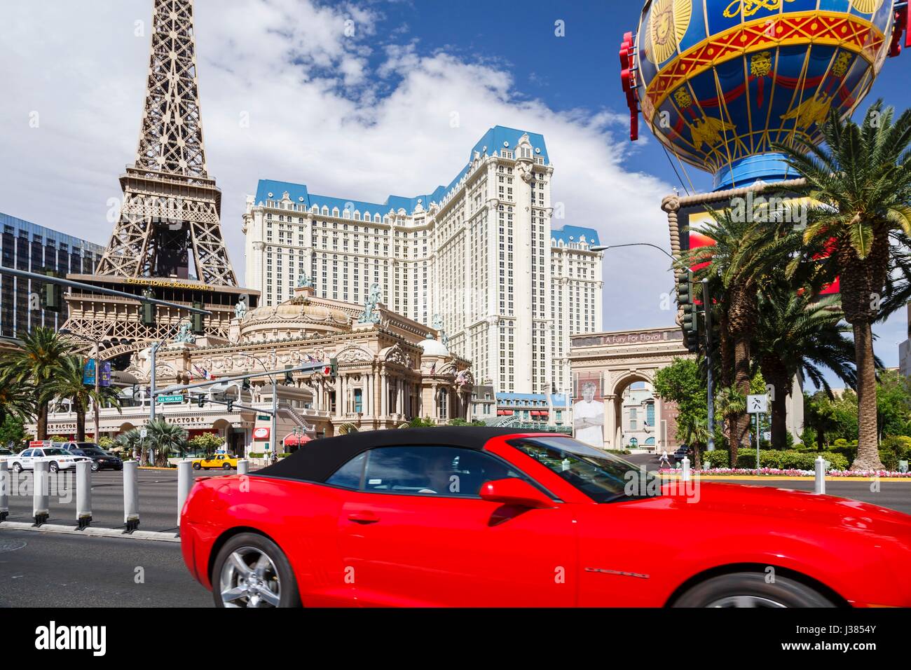 A red convertible rental car drives by Paris Las Vegas Hotel on Las Vegas Boulevard Stock Photo