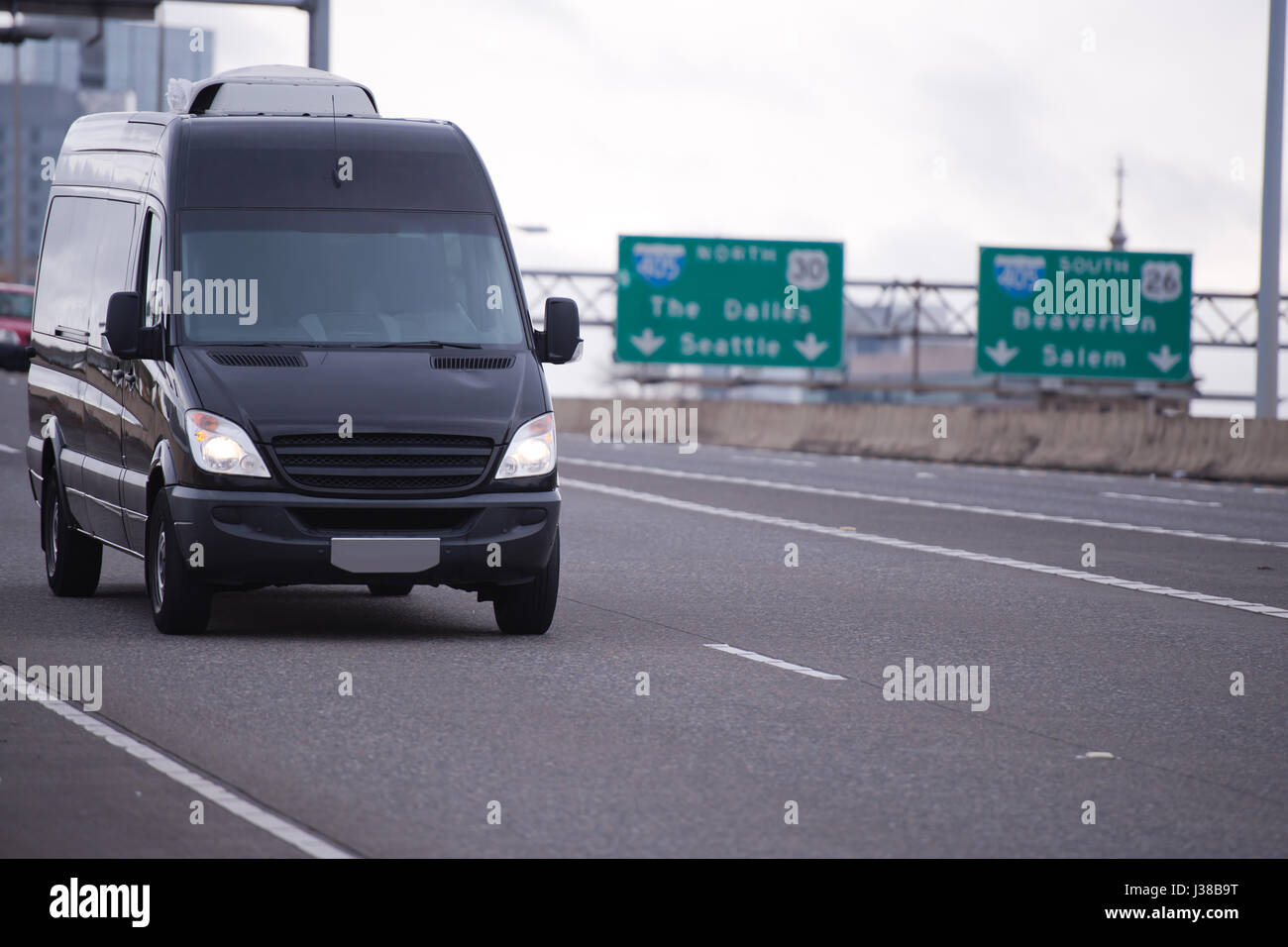 The compact black mini van for the transport of commercial goods and parcels, as well as for use in a small business, traveling on the wide highway Stock Photo
