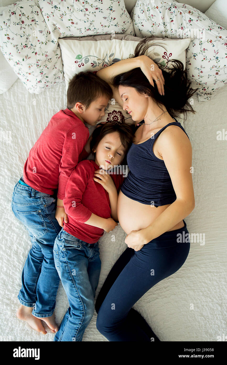 Beautiful pregnant young mother and her two children, boys, lyign in bed at home Stock Photo