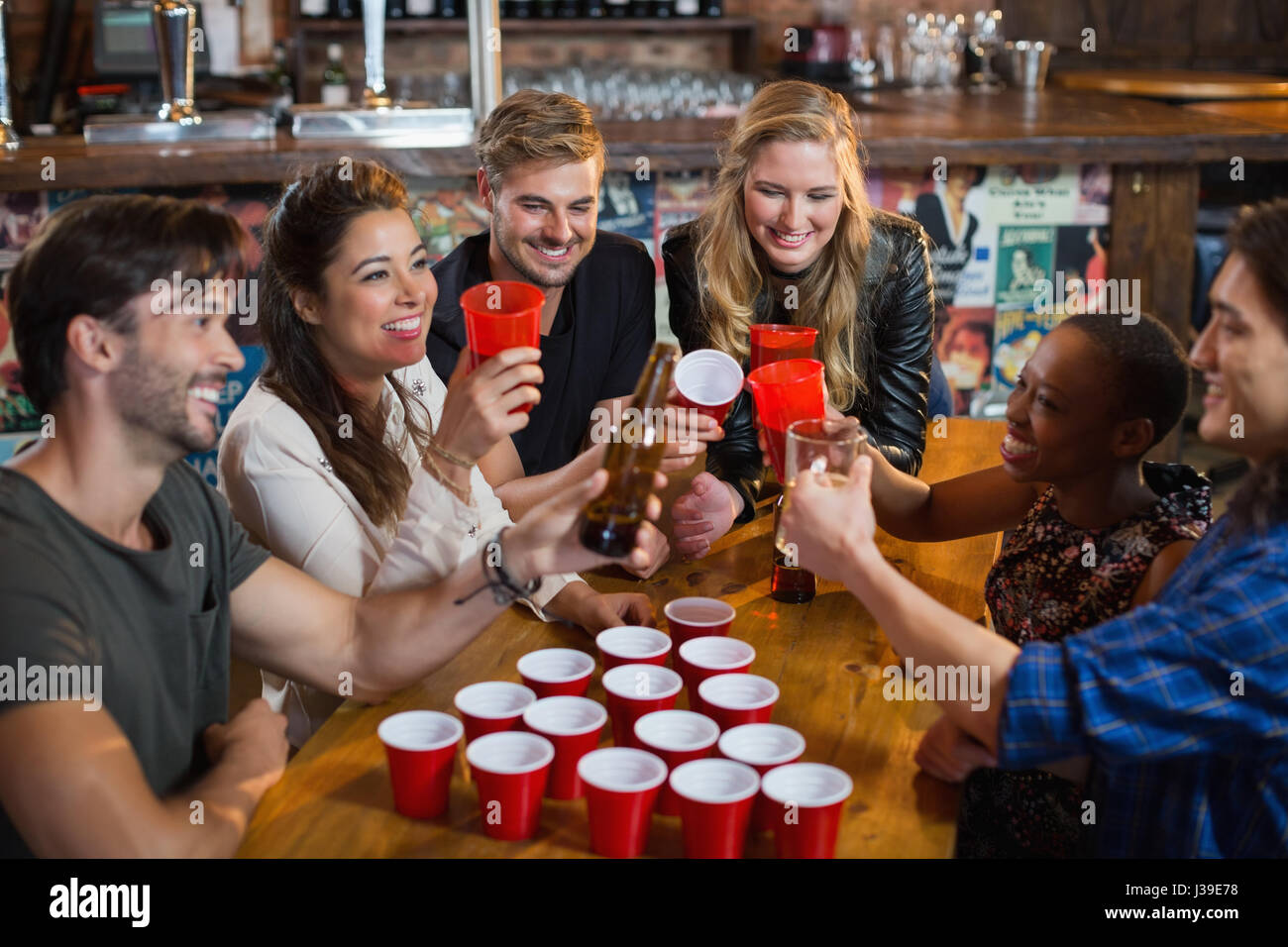 Happy friends drinking beer while sitting around disposable cups on table in bar Stock Photo