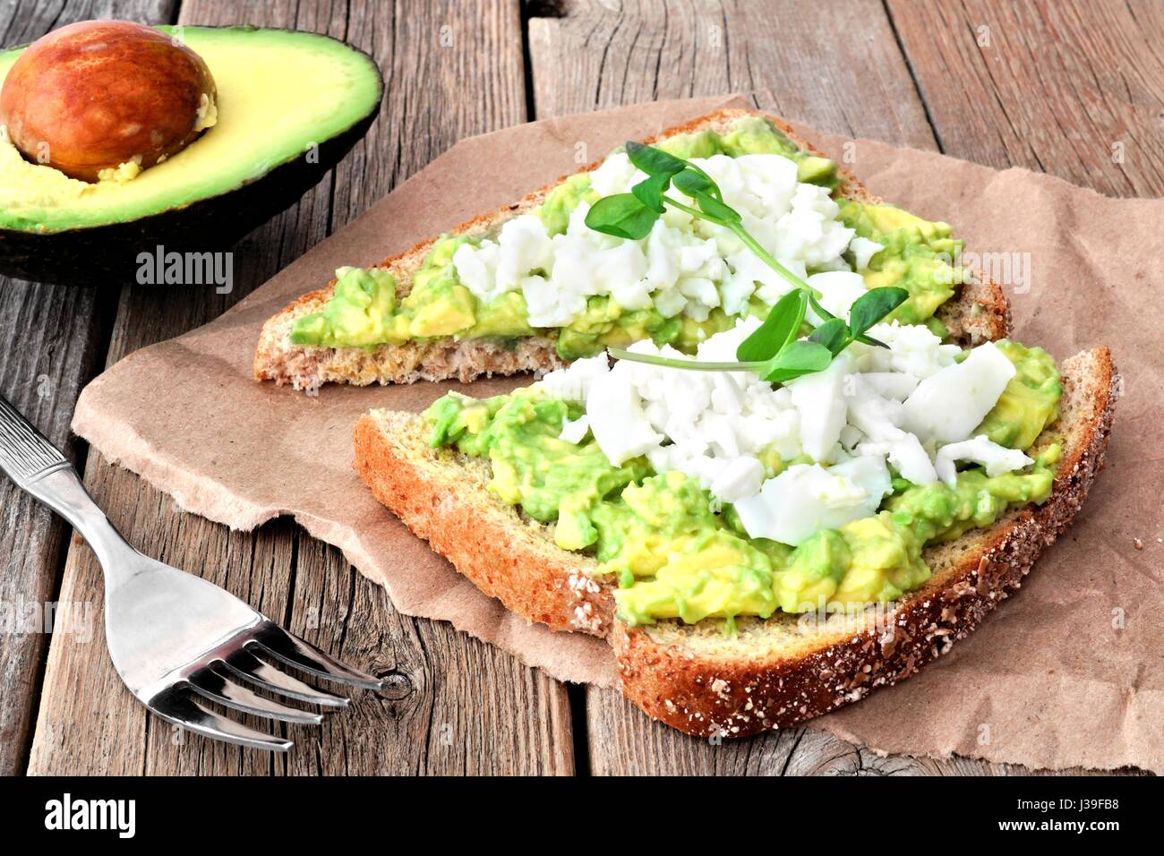 Avocado toast with egg whites and pea shoots on paper against a rustic wood background Stock Photo
