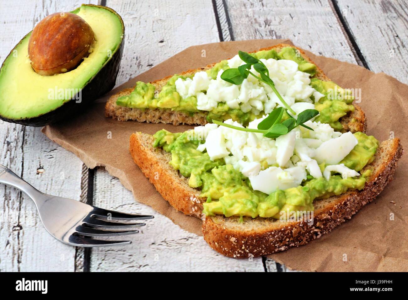 Avocado toast with egg whites and pea shoots on paper against a white wood background Stock Photo